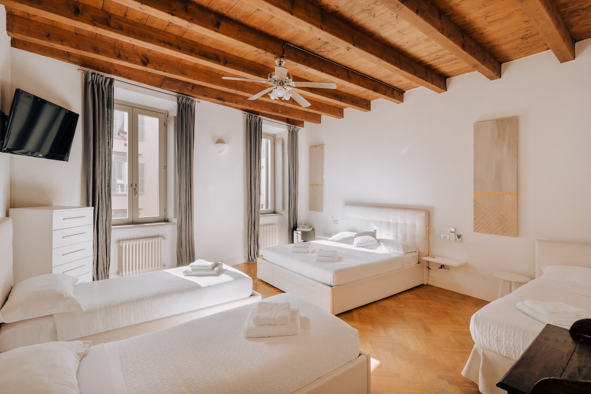 Habitació d'hotel amb dos llits, un ventilador de sostre, televisió i una finestra amb cortines.