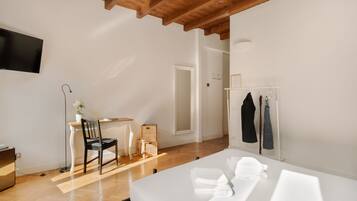Een moderne hotelkamer met een houten plafond, een flatscreen televisie aan de muur, een bureau met stoel, een bed met netjes opgevouwen handdoeken en een kledingkast met hangende kleding.