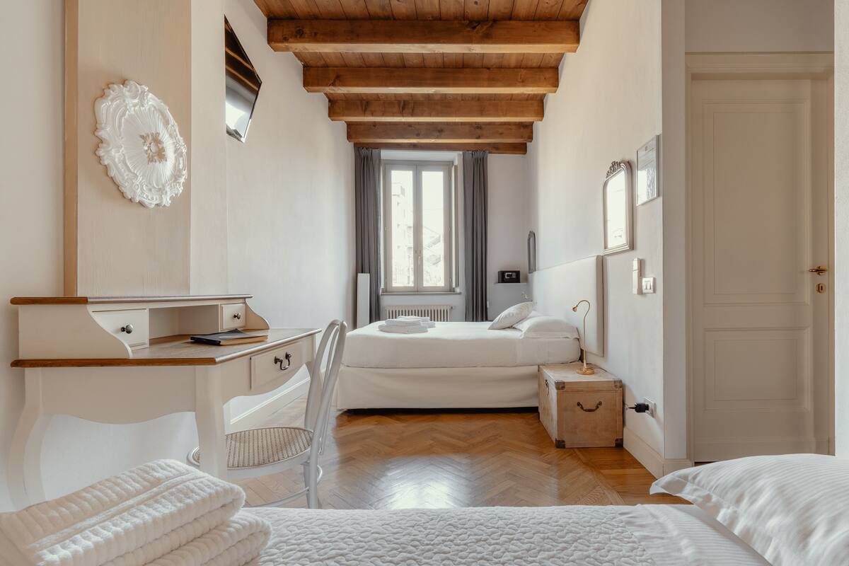 Un dormitori amb sostre de fusta, un llit, un escriptori, una cadira i una finestra amb cortines.