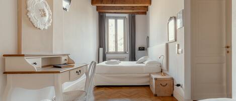 Quarto com teto de madeira, uma cama, uma escrivaninha, uma cadeira e uma janela com cortinas.