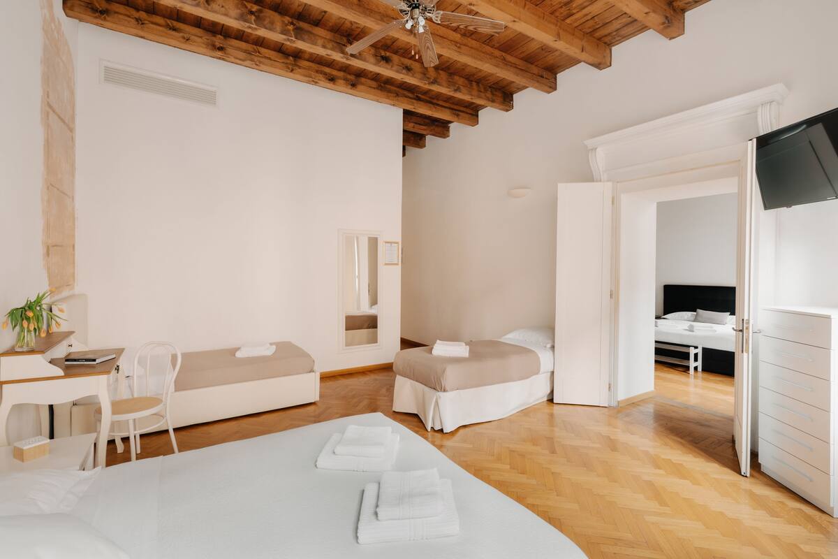 Habitació d'hotel moderna amb sostre de fusta, un llit amb roba de llit blanca, una taula de treball amb una cadira i un televisor penjat a la paret.
