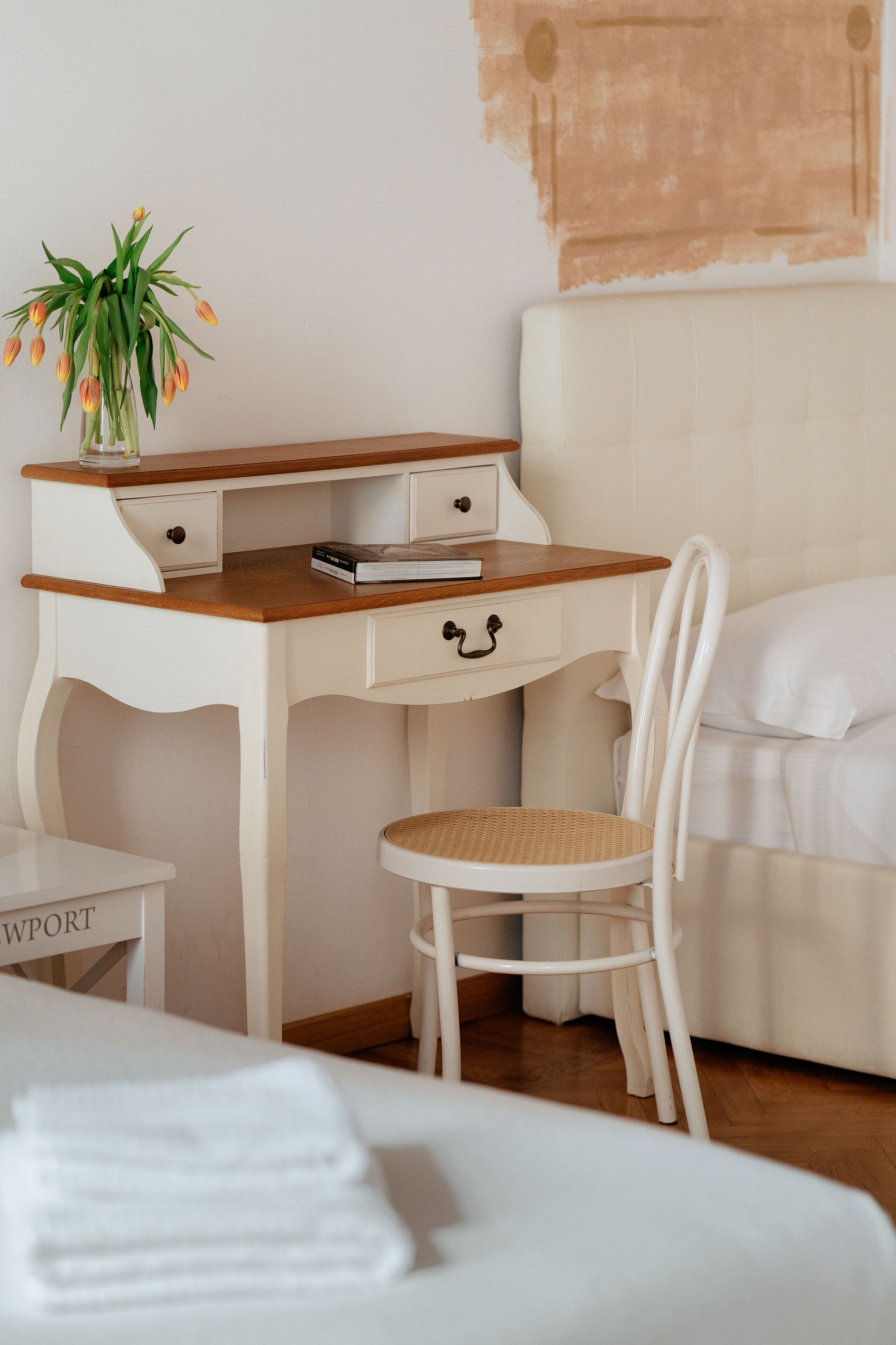 A bedroom with a wooden desk, a white chair, a bed, and a small table with a plant.