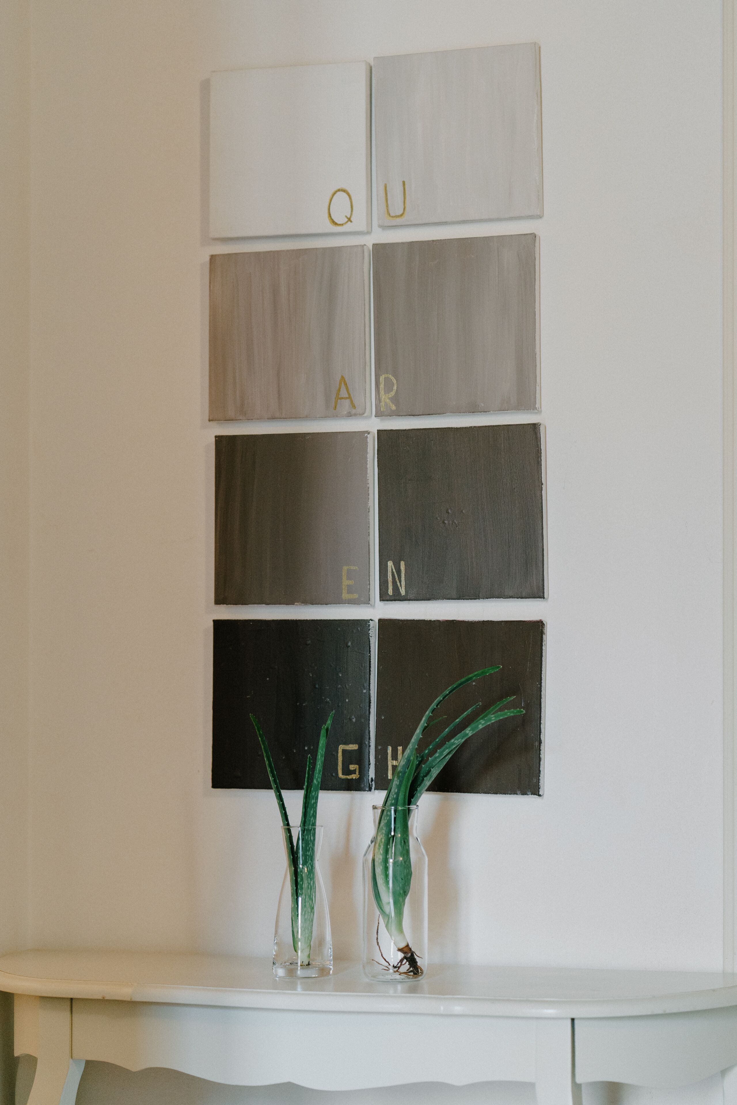 A wall with a grid of panels, each with a letter, spelling out a word. Below the panels, there are two vases with green plants.