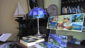 A desk with a lamp, books, a small sailboat model, and a collage of photos. - Hotel La Rondinella (Cannero Riviera)