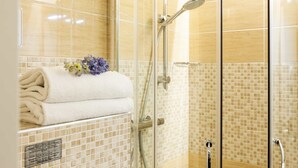 A glass-enclosed shower with a handheld showerhead, a towel rack with folded towels, and a small flower arrangement. - Prestigia Rooms B&B Firenze (Florence)