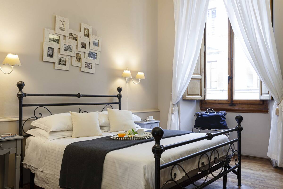 Un lit bien fait, avec un plateau contenant des articles pour le petit-déjeuner, une table de chevet avec une lampe et un mur décoré de tableaux encadrés.