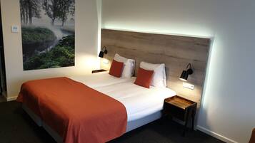 Une chambre d’hôtel avec un grand lit, deux tables de chevet avec des lampes, une tête de lit et une grande fresque murale sur le thème de la nature.