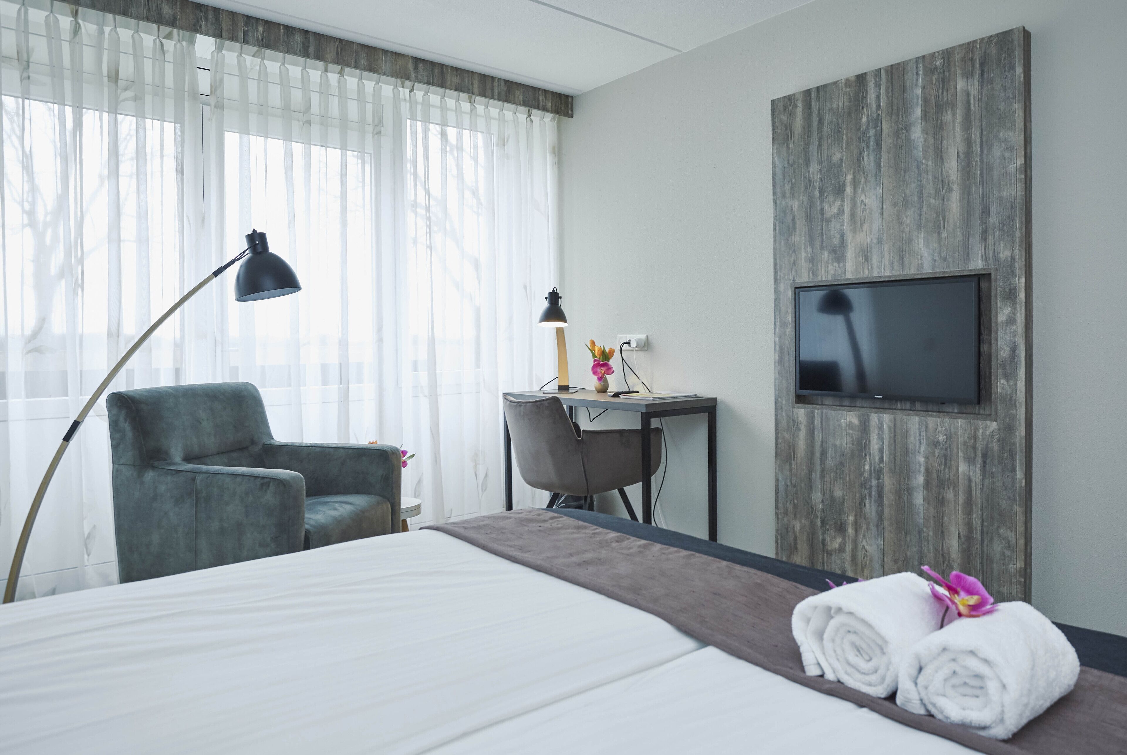 Een hotelkamer met een bed, een bureau, een stoel, een televisie en een lamp.
