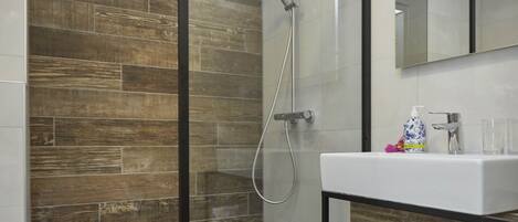 A modern bathroom with a glass-enclosed shower, a wooden wall, a white sink, and a mirror above it.