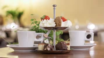 A three-tiered dessert stand with cakes and strawberries, accompanied by white cups on saucers.