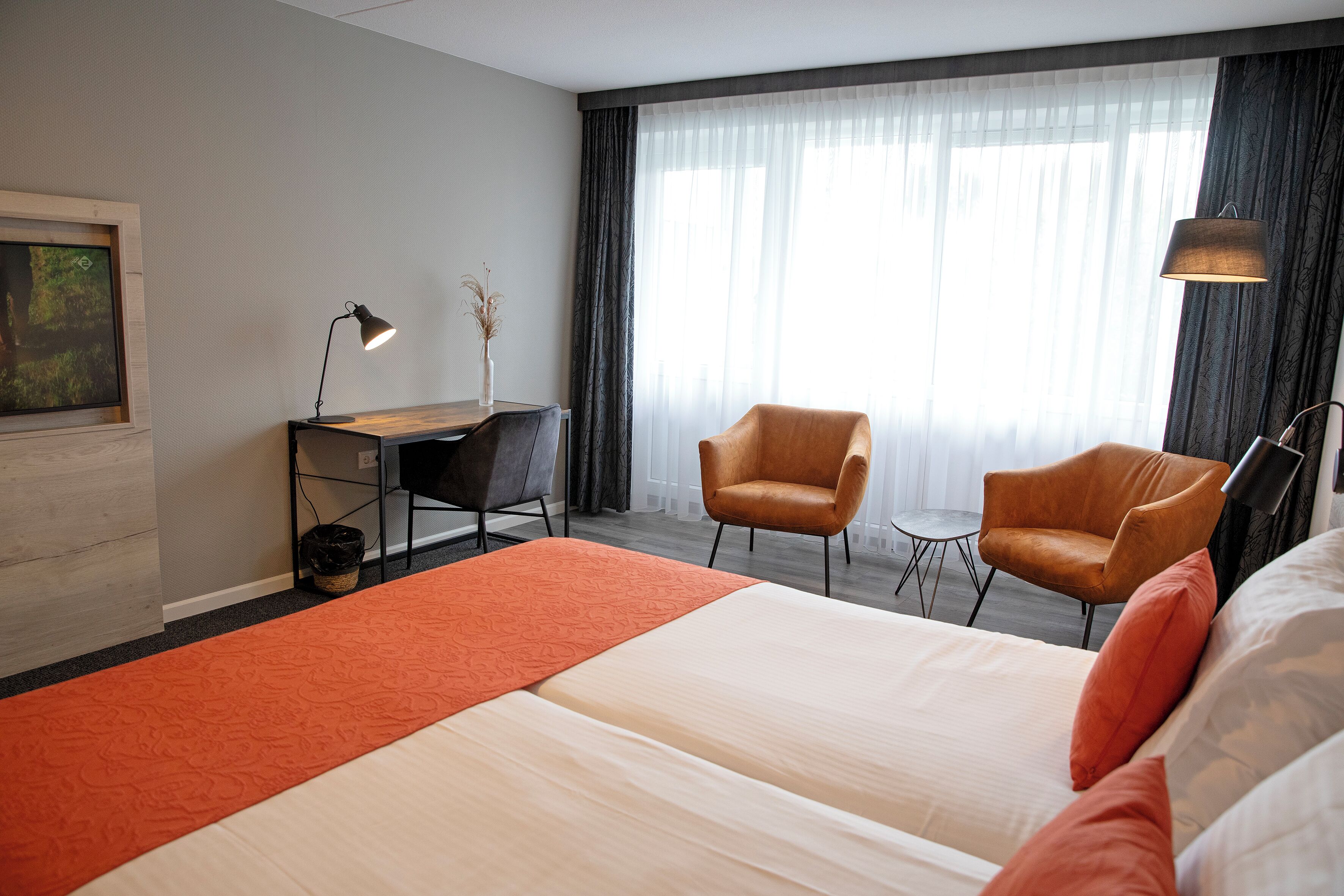 A hotel room with a large bed, two armchairs, a desk, and a lamp.