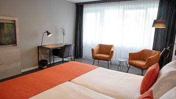A hotel room with a large bed, two armchairs, a desk, and a lamp.