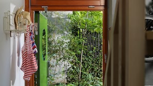 A wooden door leading to a garden with a green door, a wicker basket, and a pair of yellow sandals on a wooden deck. - Ohboy Hotell (Malmö)