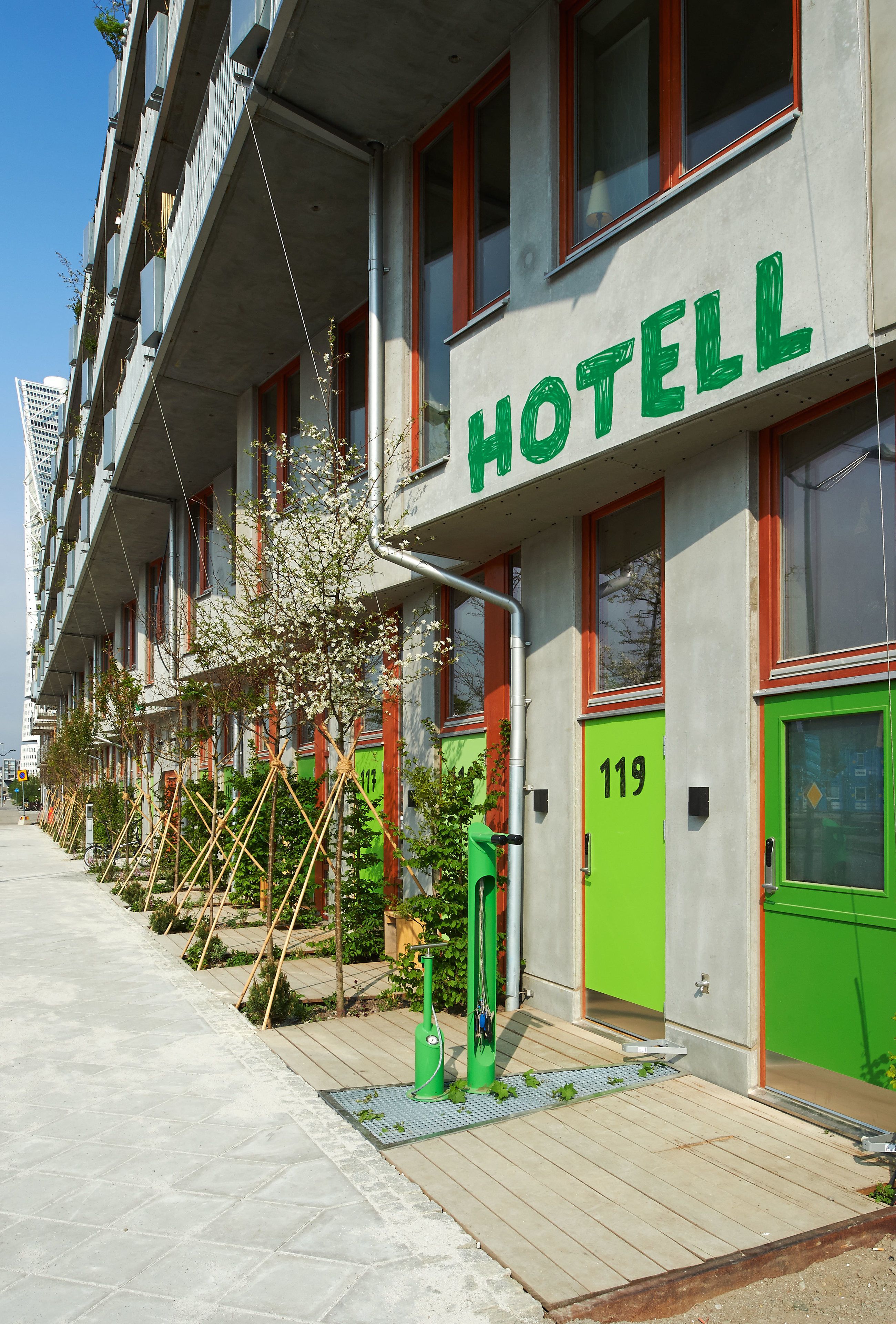 Un hotel con un letrero verde, número 119, que presenta un diseño moderno con ventanas de marco rojo y fachada de concreto.