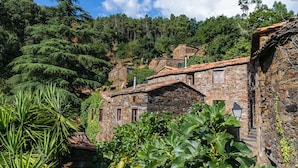 A stone building with a tiled roof, surrounded by lush greenery and trees. - Cerdeira - Home for Creativity (Lousa)
