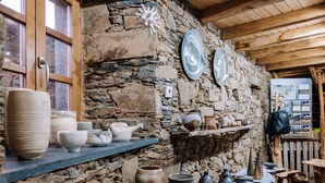 A rustic interior with stone walls, wooden beams, and shelves displaying pottery and ceramics. - Cerdeira - Home for Creativity (Lousa)