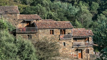 A stone building with multiple balconies and terracotta tiled roofs, surrounded by dense forest.