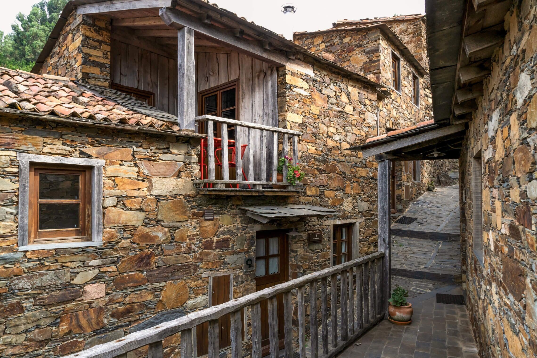 Un bâtiment en pierre doté d’un balcon en bois, d’une petite porte et d’une ruelle étroite.