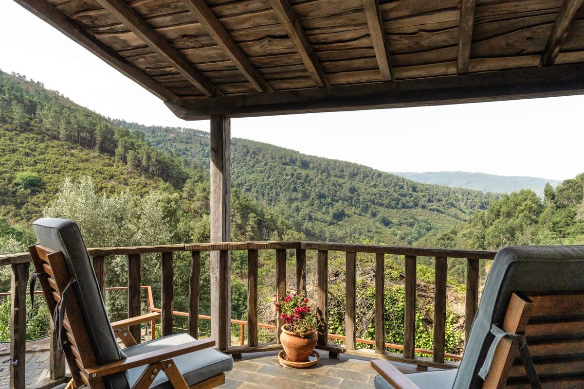 A wooden deck with two lounge chairs and a potted plant, overlooking a forested valley.