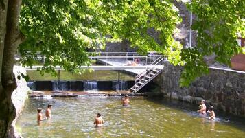 A natural pool with a waterfall, surrounded by stone walls and trees.