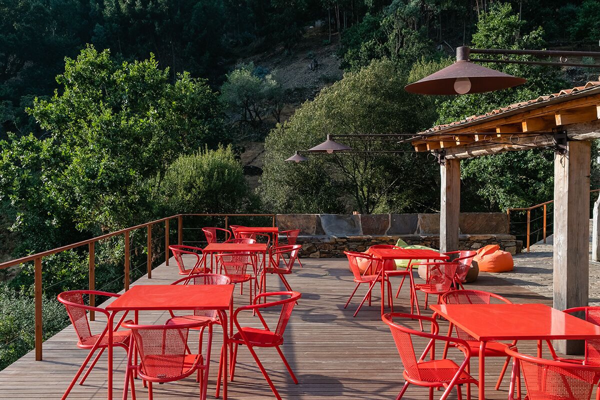 An outdoor patio with red metal tables and chairs, a stone wall, and a wooden pergola with hanging lamps.
