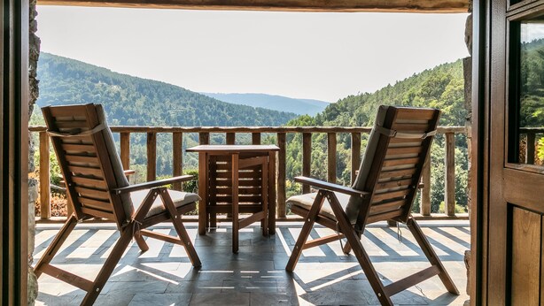 A wooden deck with two chairs and a table, overlooking a mountainous landscape. - Cerdeira - Home for Creativity (Lousa)