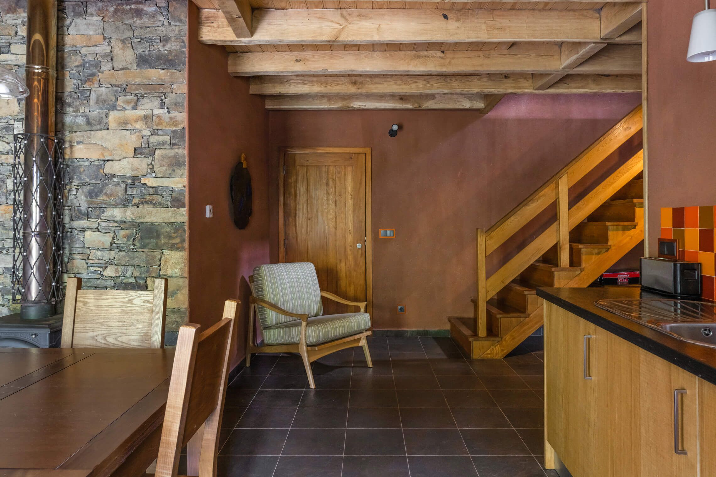 A cozy kitchen with a stone wall, wooden ceiling, and a chair.