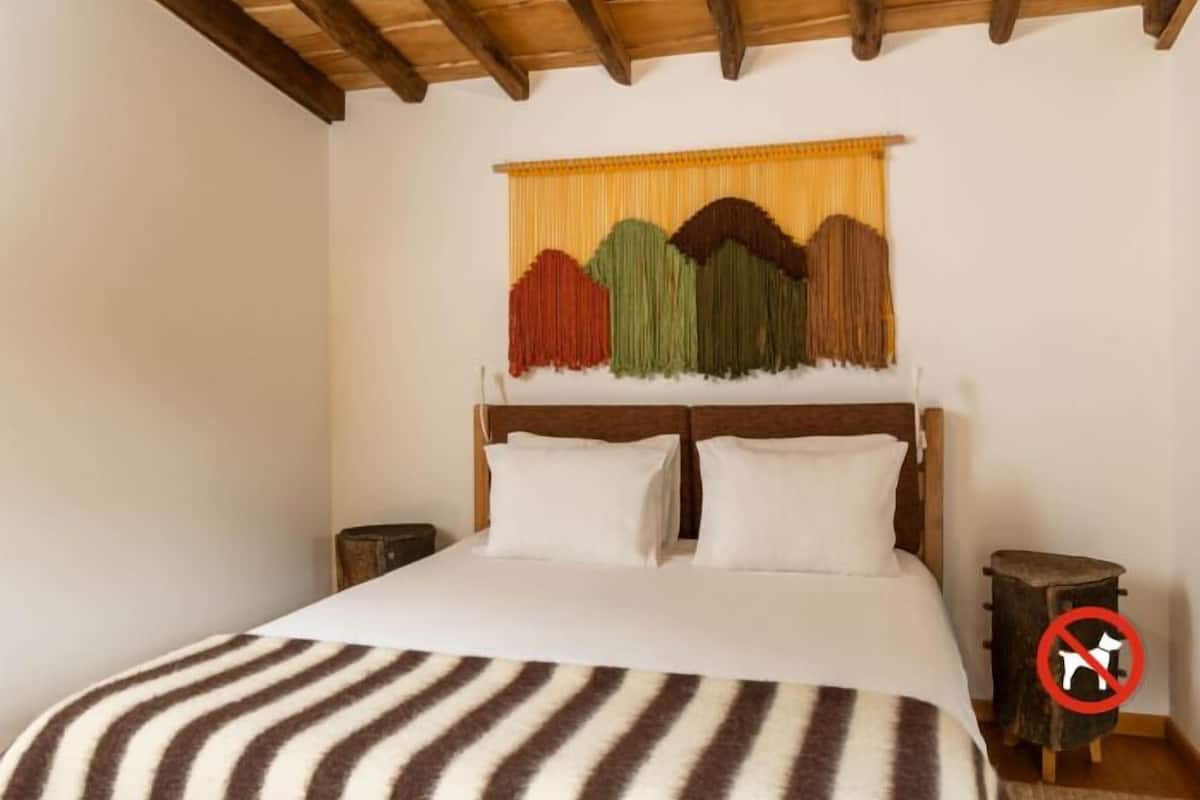 A bedroom with a wooden headboard, a bed with white bedding, and a colorful tapestry on the wall.