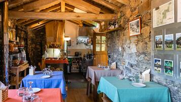 A rustic dining area with stone walls, wooden beams, and tables set for dining.
