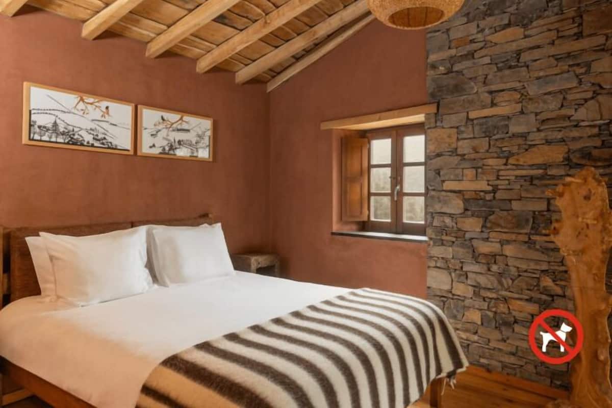 A bedroom with a wooden bed, a stone wall, and artwork on the wall.