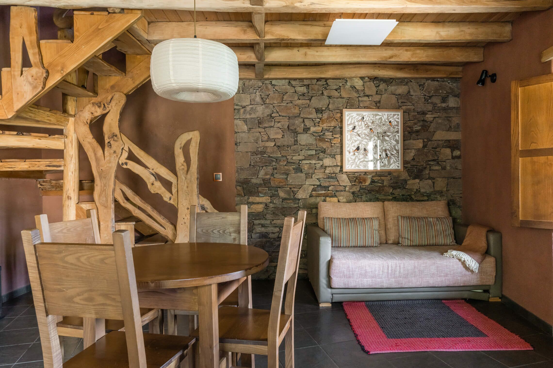 Interior rústico com parede de pedra, móveis de madeira e escada.
