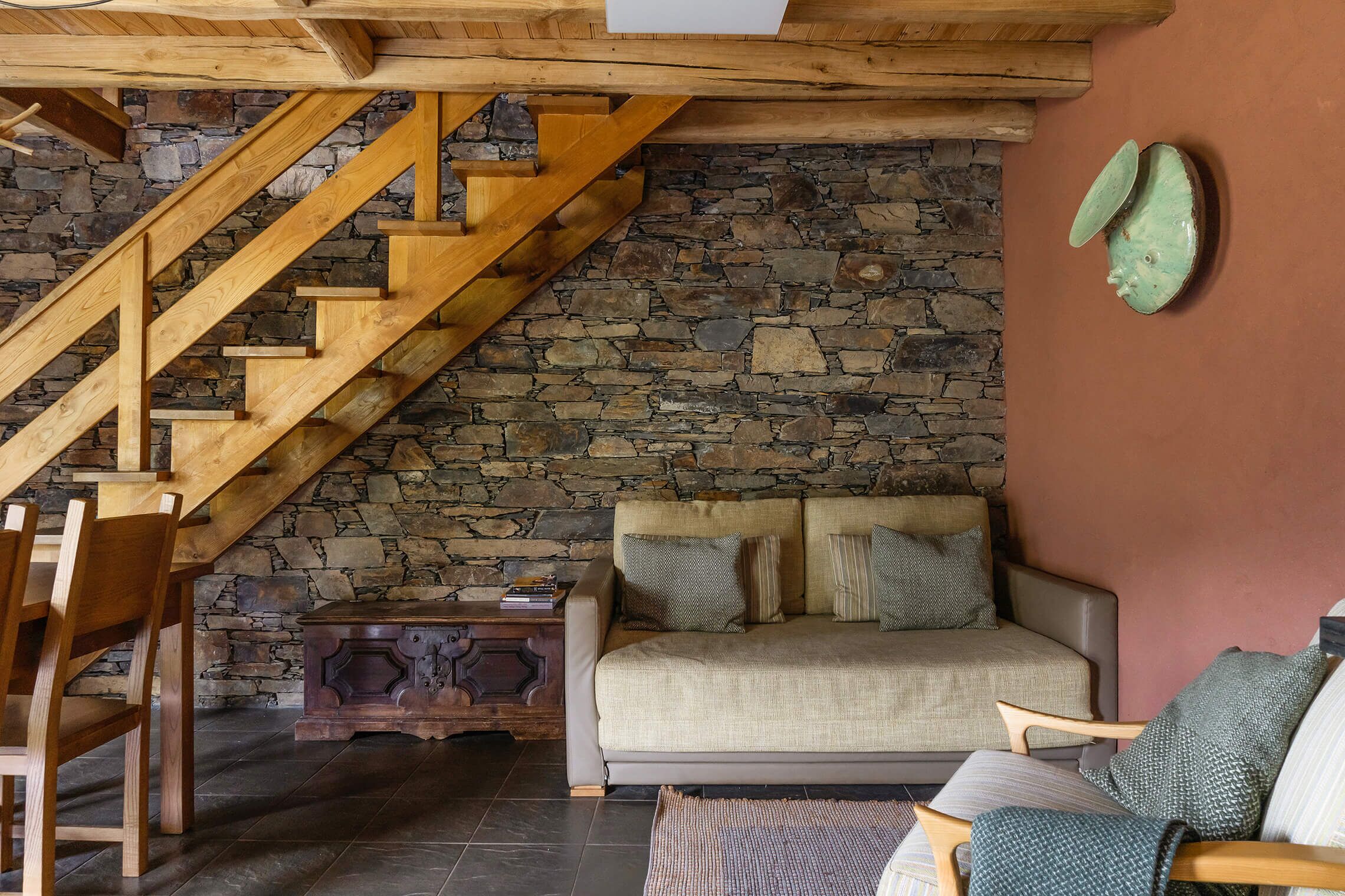 Une pièce chaleureuse avec un mur en pierre, un escalier en bois et un canapé agrémenté de coussins.