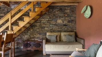 Une pièce chaleureuse avec un mur en pierre, un escalier en bois et un canapé agrémenté de coussins.