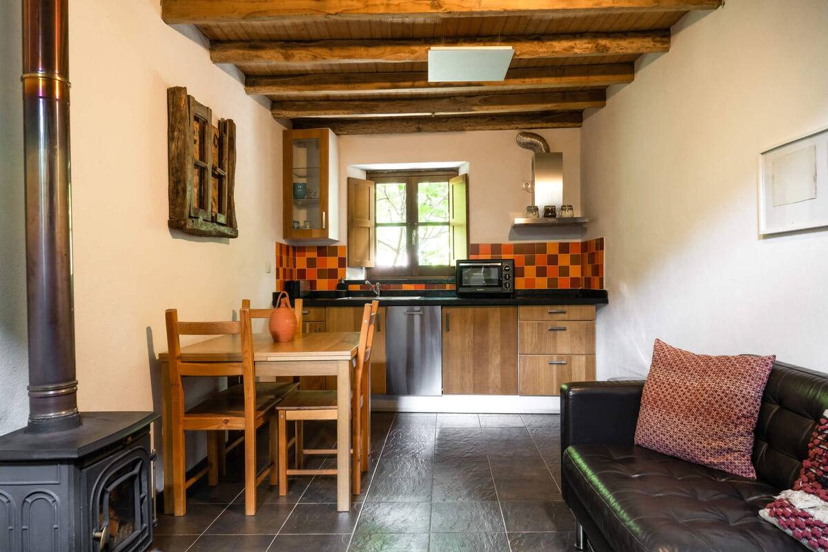 A cozy living room with a fireplace, a dining area with wooden furniture, a kitchen with a microwave and wooden cabinets, and a black leather sofa with patterned cushions.