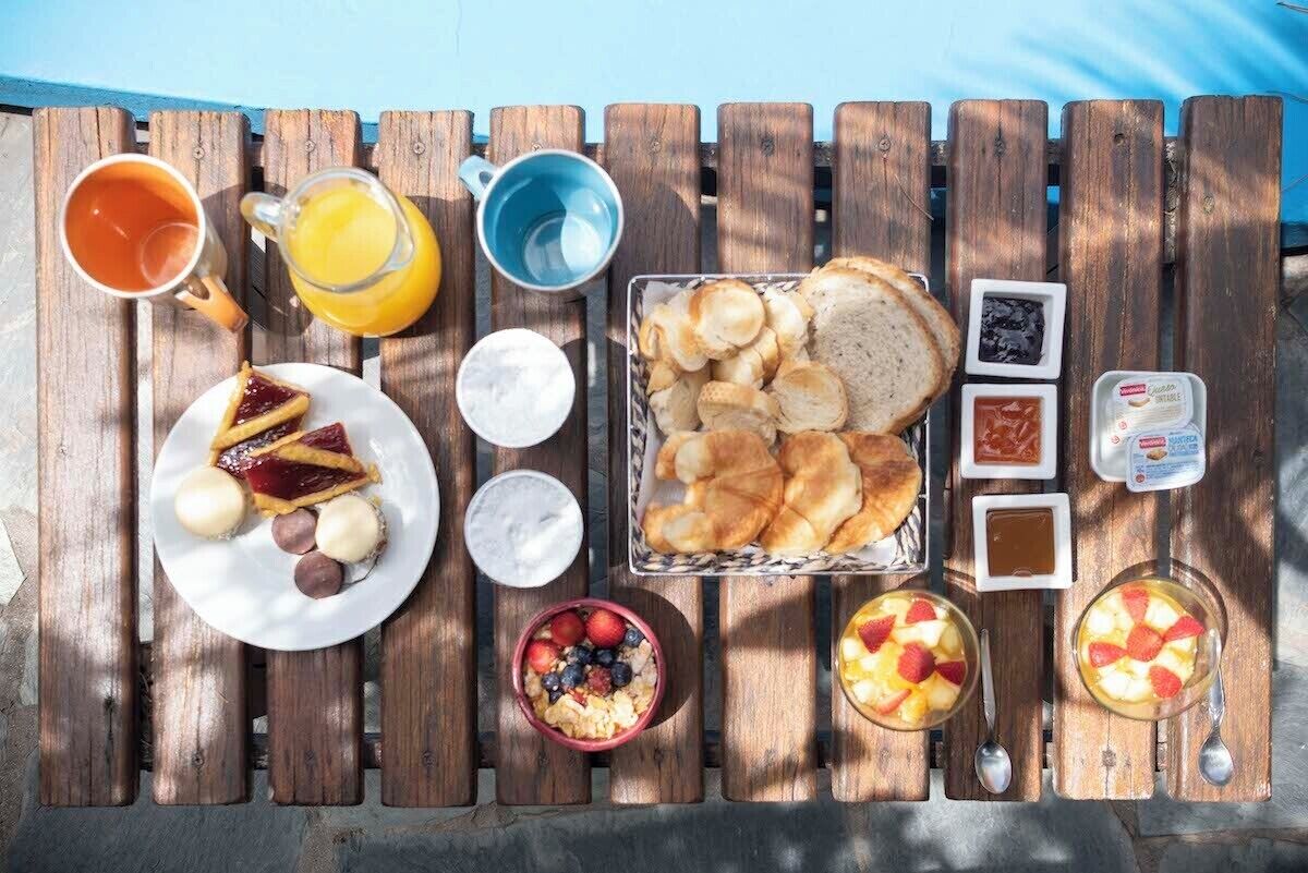 Una mesa de madera con productos para el desayuno, como tostadas, pasteles, fruta y bebidas.