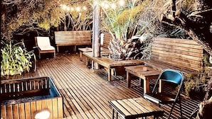 An outdoor wooden deck with benches and chairs, surrounded by plants and trees. - Posada del Viento (Tandil)