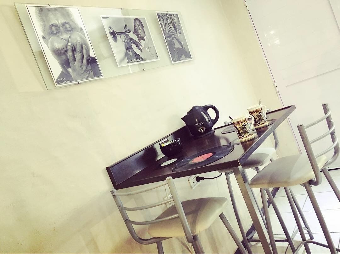 Un coin repas avec une table, des chaises, une bouilloire et une tasse à café. Des tableaux encadrés ornent le mur.
