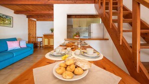 Ein gemütliches Wohnzimmer mit einer Holztreppe, einem Esstisch mit Gebäck und einer Küche im Hintergrund.