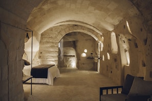 Una habitación rústica de piedra con una cama, un sillón y una mesita.