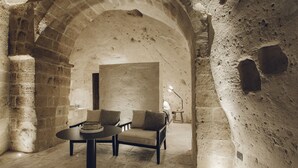 A room with a stone wall, a table with a chair, and a lamp.