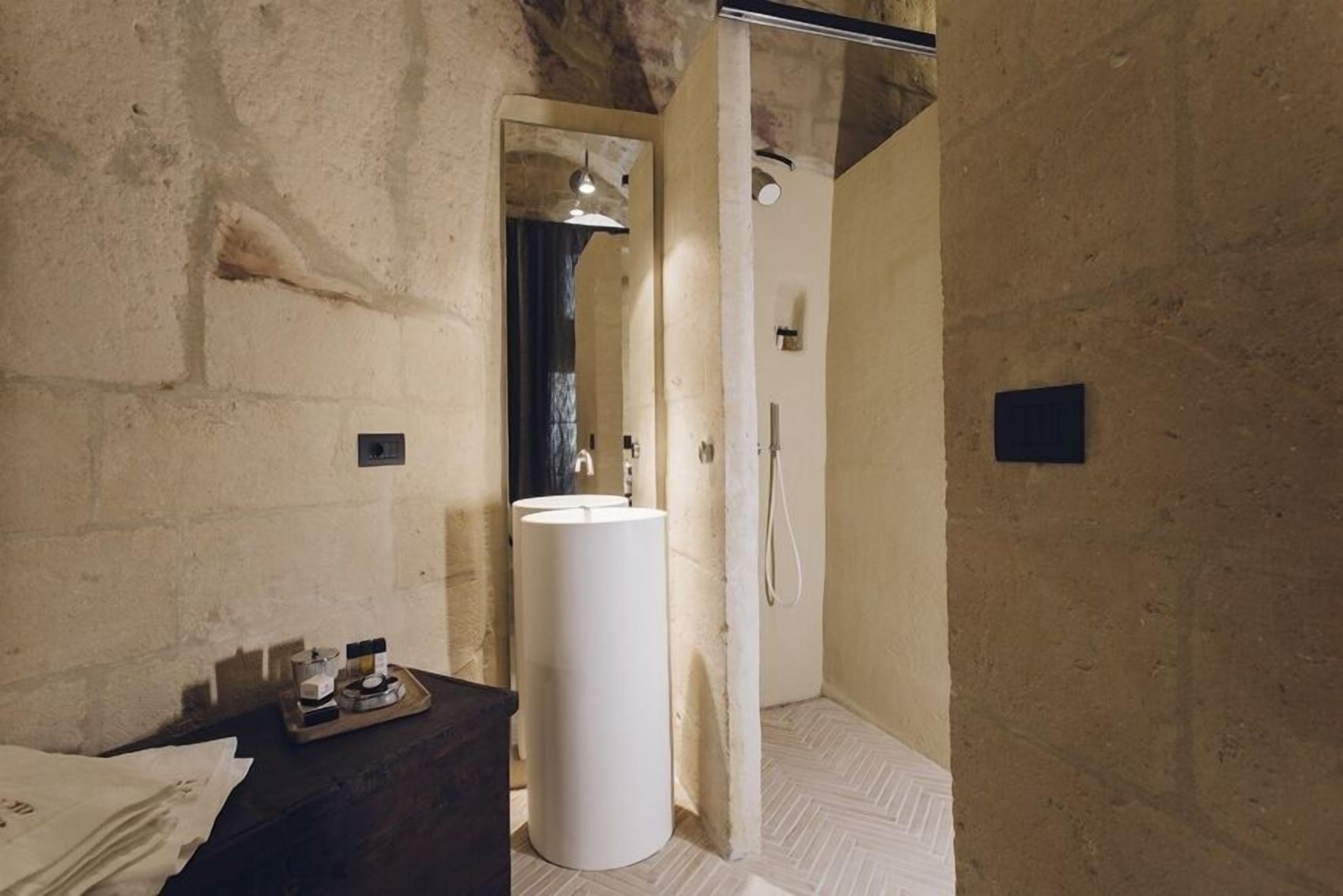 A bathroom with a large white sink, a glass shower enclosure, and a wooden vanity with toiletries.