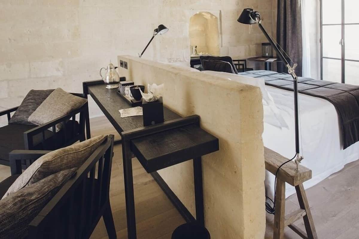 A hotel room with a wooden desk, a bed, a chair, and a lamp.