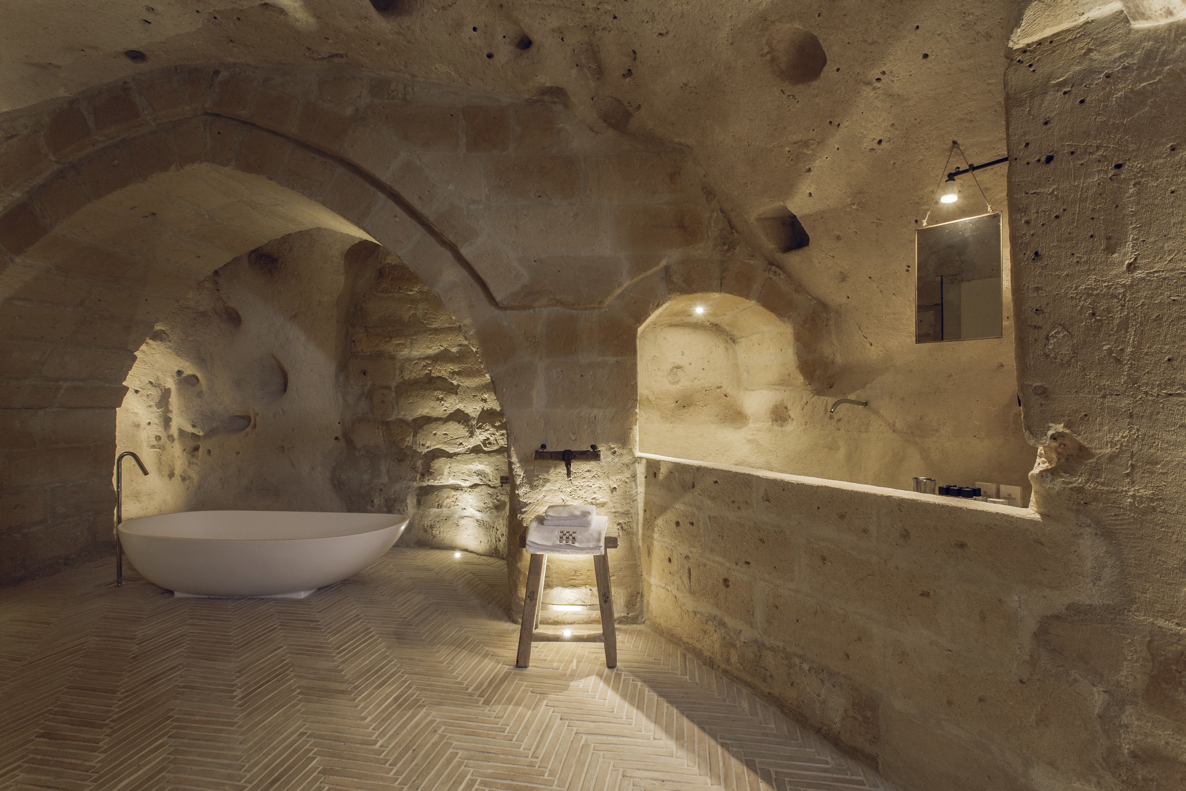 Ein Badezimmer mit Steinwänden, einer freistehenden Badewanne, einem kleinen Hocker und einem Spiegel an der Wand.