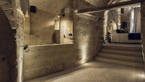 A stone-walled room with a herringbone-patterned floor, a bed, and a small table with a lamp. - Il Palazzotto (Matera)