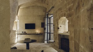 A stone-walled room with a round table, a bench, and a fireplace. - Il Palazzotto (Matera)