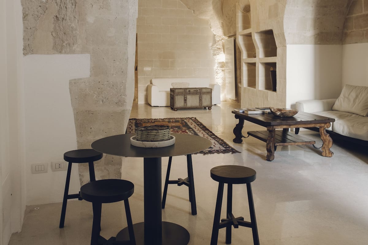 A spacious room with a stone wall, a round table with stools, a wooden coffee table, and a white sofa.
