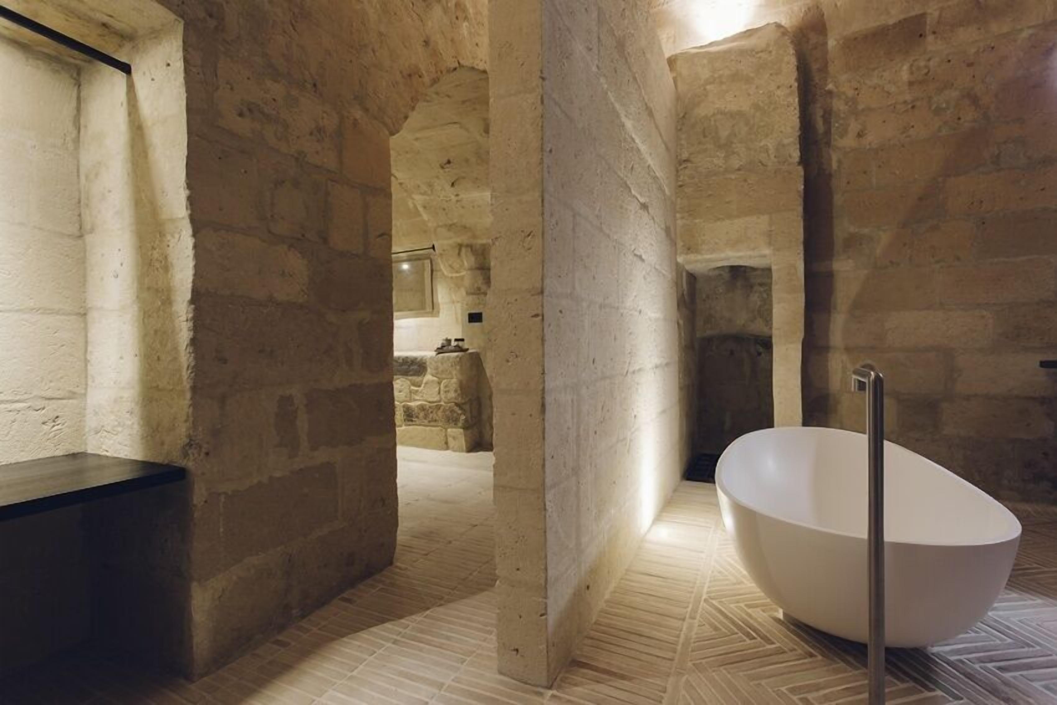Ein modernes Interieur mit einer freistehenden Badewanne, Steinwänden und einer Sitzbank.