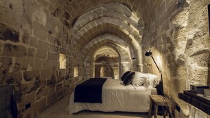 A room with a bed, a wooden bench, and stone walls. - Il Palazzotto (Matera)