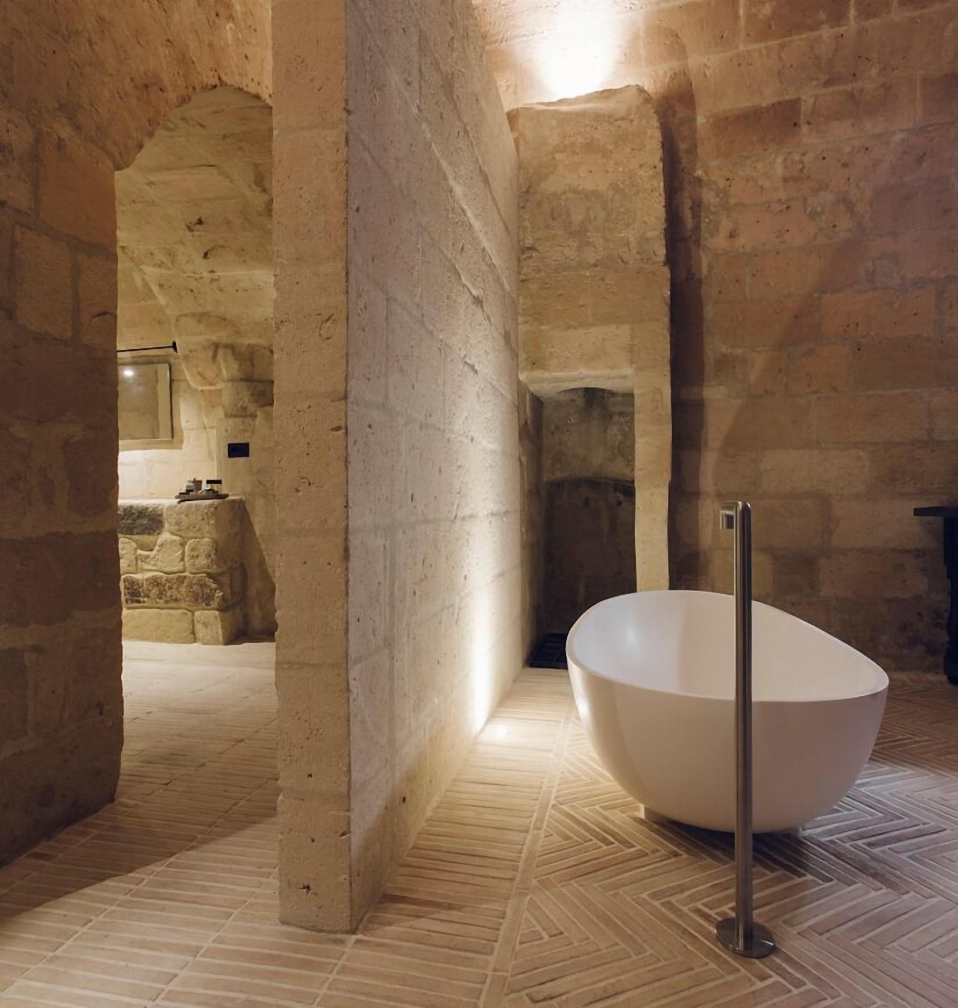Una habitación con paredes de piedra, una bañera blanca grande y suelo con estampado en espiga.