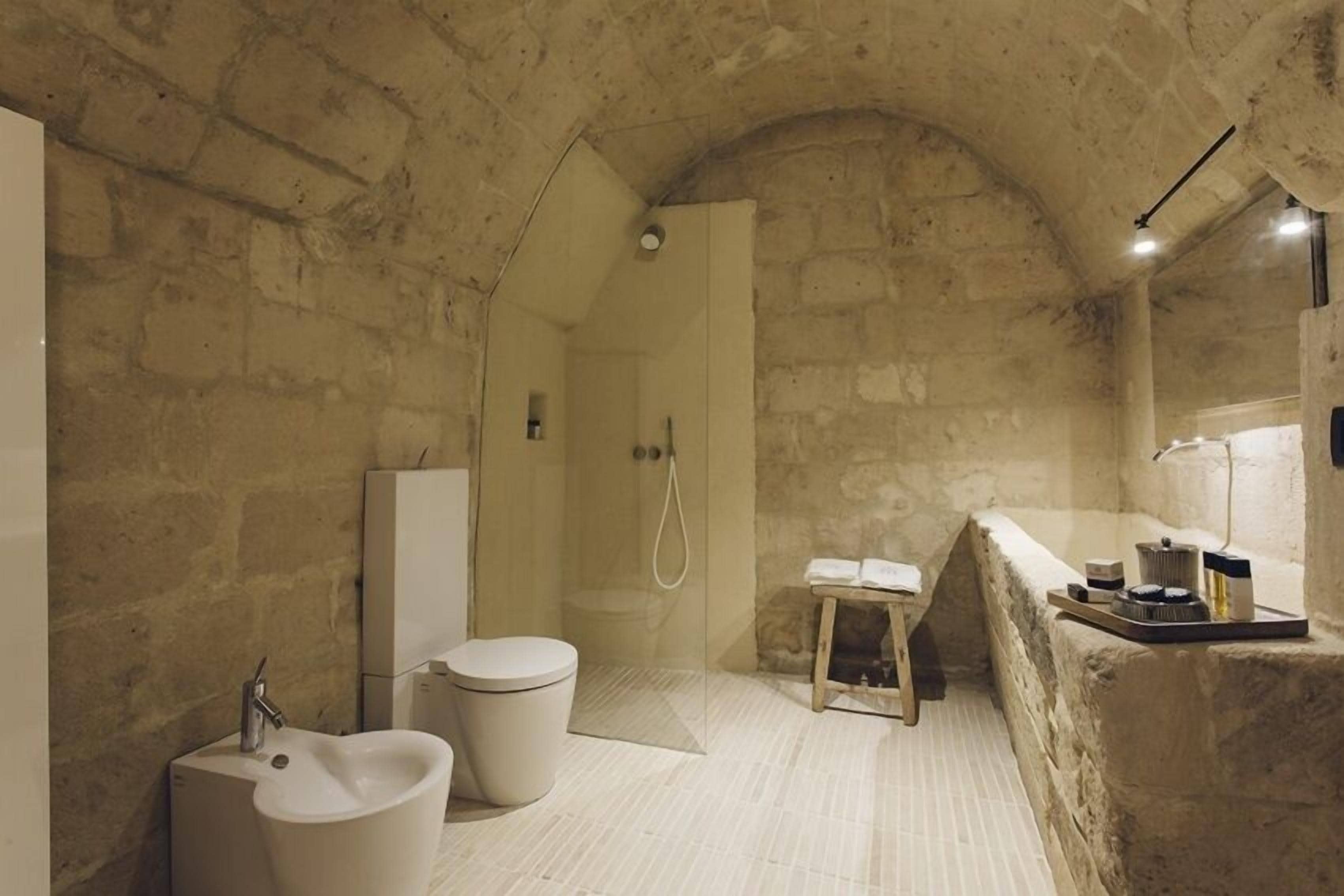 Un baño con paredes de piedra, ducha, lavamanos e inodoro.